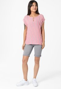 Striped short-sleeve top in pink and white with a keyhole neckline, paired with rolled grey shorts and white sneakers. Smooth fabric texture.