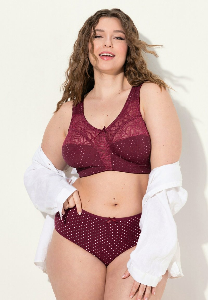 Reggiseno bordeaux con dettagli in pizzo e design a pois, abbinato a mutandine a vita alta coordinate. Texture morbida, con un elegante fiocco al centro.