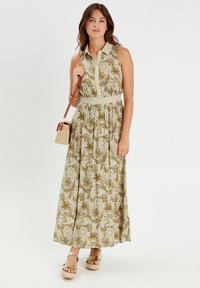 Maxi dress in a green and white floral pattern, sleeveless with a collared neckline, cinched waist, and flowy skirt. Model accessorizes with a small bag.