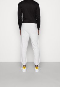 Grå svettbyxor med elastiska muddar, kombinerat med en svart långärmad skjorta. Modellen har på sig vita sneakers med gula detaljer på hälarna.