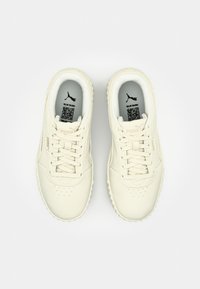 Pár krémově bílých tenisek Puma s tkaničkami, perforovanou špičkou a viditelnými QR kódy uvnitř bot na stélkách.