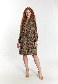 Braun gemustertes Kleid mit langen Ärmeln, Schlüsselloch-Ausschnitt und lockerer Passform. Glatte Textur, kombiniert mit hellen, spitzen Absätzen.