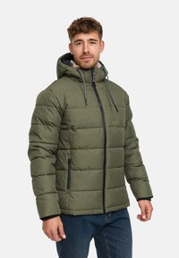 Veste rembourrée verte avec capuche, dotée de détails de fermeture éclair noirs et de cordons de serrage. Tissu texturé avec sections matelassées horizontales.