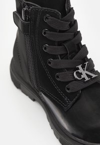 Czarne botki za kostkę o błyszczącym wykończeniu, z czarnymi sznurówkami, zamkiem błyskawicznym z boku oraz srebrnym logo "CK". Gumowa podeszwa zapewniająca przyczepność.