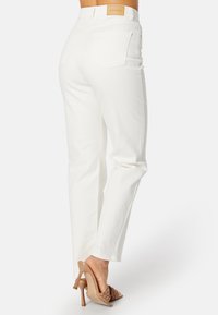 Witte denim jeans met een rechte broekspijp, voorzien van achterzakken en een bruine leren label op de tailleband. Gladde textuur, minimalistische details.