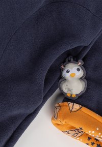 Tessuto in pile navy con un tirazip a forma di pinguino e una manica arancione caratterizzata da un motivo di stelle e foglie. Texture morbida.