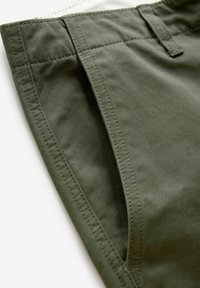 Oliven grønne stofshorts har en flad front med sidelommer, diskrete syninger og en glat tekstur.