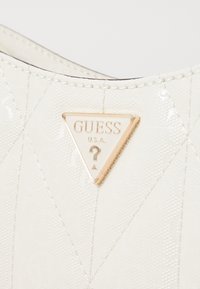 White quilted handbag made of synthetic material, featuring a gold triangle logo with "GUESS U.S.A." embossed and a raised question mark detail.
