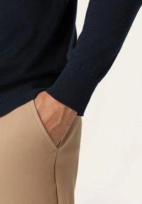 Marineblauer Pullover mit gerippten Bündchen, kombiniert mit beigen Hosen. Der Pullover hat eine glatte Textur, während die Hose eine taillierte Passform hat.