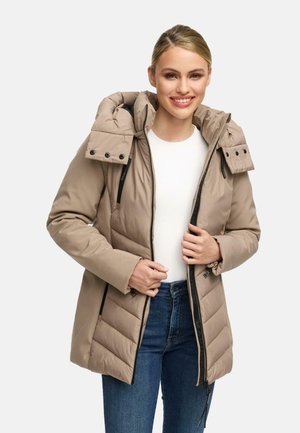 Beige pufferjack met een afneembare capuchon, voorzien van een ritssluiting, zijzakken en een gestikte structuur. Draagt over een witte top en jeans.