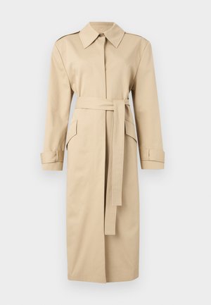 Μπεζ μακρύ trench coat με φαρδιά γιακά, μακριά μανίκια, μπροστινή ζώνη και τσέπες με καπάκι σε μονόχρωμο φόντο.