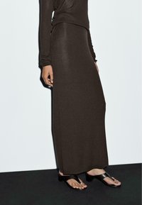 Jupe maxi en tricot côtelé marron associée à un haut à manches longues, complétée par des sandales plates noires et une finition lisse et texturée.