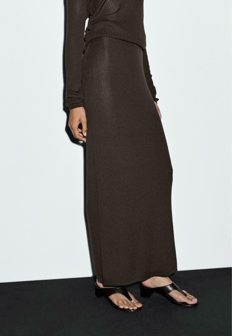 Jupe maxi en tricot côtelé marron associée à un haut à manches longues, complétée par des sandales plates noires et une finition lisse et texturée.
