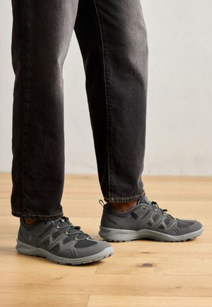 Baskets de sport grises en matériaux synthétiques et en maille, présentant une surface texturée, des lacets élastiques et un design de semelle amortissante.