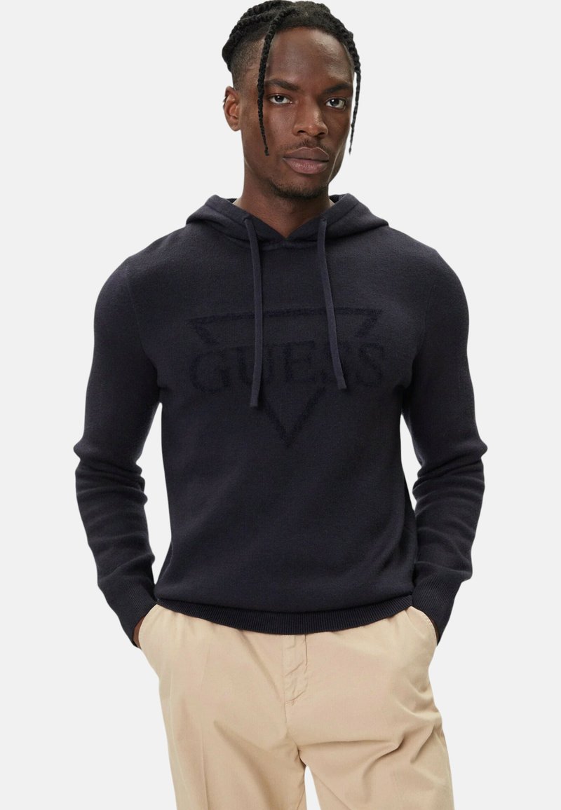 Felpa con cappuccio blu navy in tessuto liscio, con un logo "GUES" in rilievo tono su tono all'interno di un triangolo ben visibile. Polsini e orlo aderenti.
