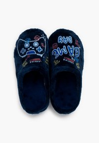 Tmavě modré huňaté pantofle s plochým designem. Obsahují grafiku herního ovladače a barevný text s nápisem „DEN HRY“ a souvisejícími frázemi.