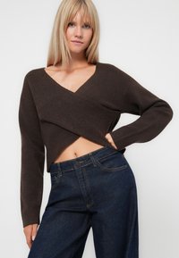 Pull en wrap marron en matériau doux avec un col en V, des manches longues et une coupe courte, associé à un jean en denim noir taille haute.