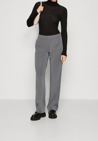 Pantalons gris à jambes larges avec taille élastique, accompagnés d'un turtleneck noir à manches longues. Des chaussures noires ajoutent un détail contrastant.