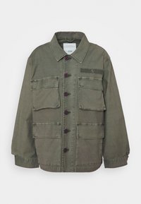 Jasnozielona kurtka zapinana na guziki z czterema przednimi kieszeniami z klapkami, kołnierzykiem i długimi rękawami, ułożona płasko na białym tle.