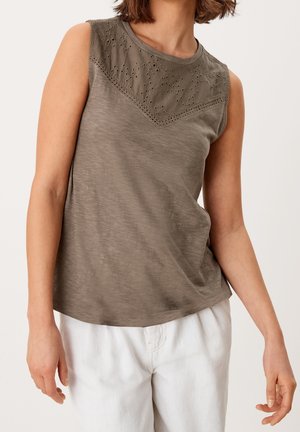 Ærmeløs olivengrøn top med øjelysblonde i overdelens del kombineret med løse hvide bukser på en stående person mod en ensfarvet baggrund.