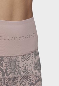 Detail pasu a horní části boků v mauve legínách s potiskem a logem „Stella McCartney“ na širokém pásku.