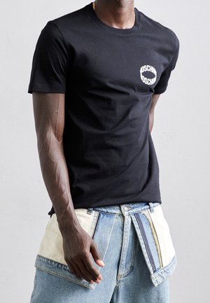 Zwarte katoenen t-shirt met een ronde halslijn en wit cirkelvormig logo op de linkerkant van de borst, gecombineerd met lichtblauwe denim broek met patchworkdetails.