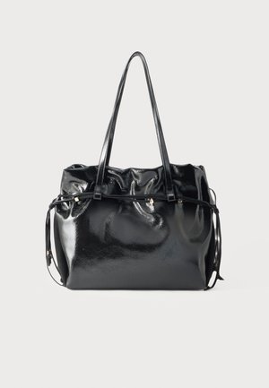 Sac cabas en cuir noir brillant avec de longues bandoulières et un détail coulissant autour du haut, sur un fond gris clair.
