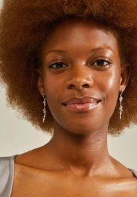 Orecchini a goccia in argento con perline verdi, caratterizzati da un design delicato. Il modello ha la pelle di colore marrone medio e capelli naturali e voluminosi.