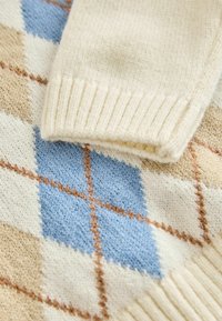 Gebreid sweater met een beige, blauwe en crèmekleurige ruitpatroon. De manchet is geribbeld en crèmekleurig, met een zachte textuur.