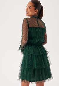 Robe verte à couches en matériau transparent avec des pois, présentant des étagères froncées, des manches longues et une taille cintrée.