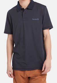 Camiseta polo azul marino hecha de algodón, con una tapeta abotonada, mangas cortas y un pequeño logotipo de Timberland en el lado izquierdo del pecho.