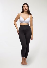 Leggings neri a vita alta abbinati a un bralette bianco. I leggings presentano una texture liscia, mentre il bralette ha spalline regolabili.