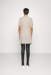 Sukienka z krótkim rękawem w beżowo-brązową kratkę, dopasowana w talii, w połączeniu z czarnymi botkami za kolano.