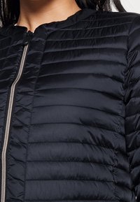 Navy puffer jacket with horizontal stitching, zip front, and a stand collar. Smooth, lightweight fabric with a slight sheen.