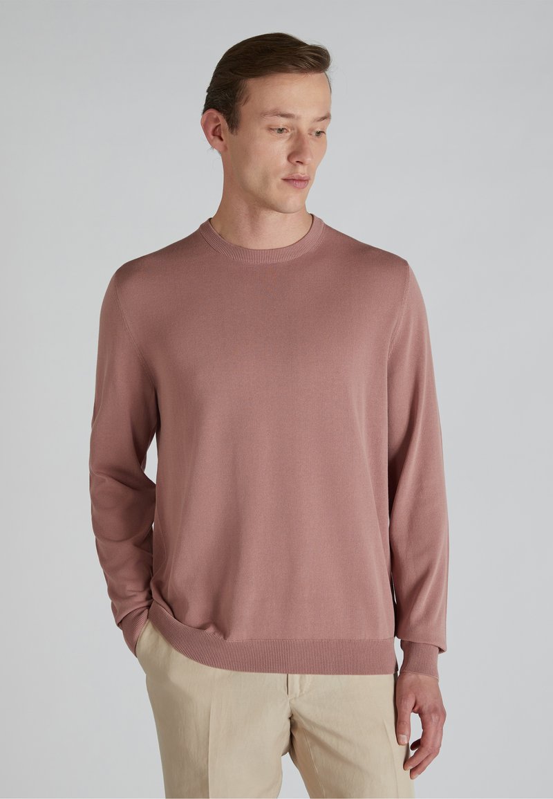 Maglione a maniche lunghe rosa chiaro con collo rotondo, realizzato in tessuto morbido, con polsini e orlo a costine, abbinato a pantaloni beige.