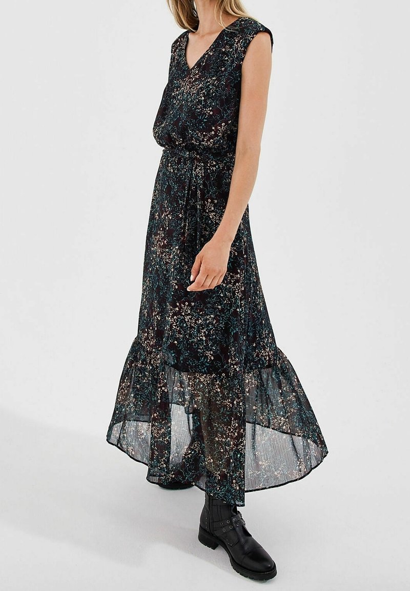 Robe maxi fluide à fleurs sombres avec des manches courtes, un décolleté en V et un bas superposé en tulle. Portée avec des bottines noires.
