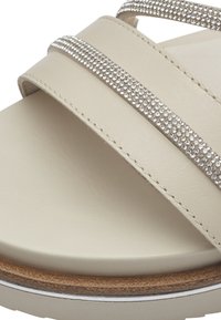 Sandalo beige con tre cinturini scintillanti decorati con strass argento, suola imbottita e un plantare in legno. Design piatto.