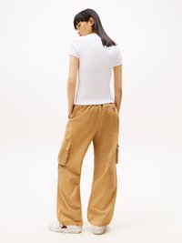 Bílá upnutá trička, lehký materiál, krátké rukávy, v kombinaci s volnými béžovými cargo kalhotami, dvě postranní kapsy a bílé tenisky s barevnými akcenty.