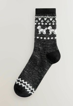 Melna zeķu pāris ar balta suņa rakstu, dimanta formām un zigzaga akcentiem. Izgatavotas no teksturētas adītas materiāla, potītes garumā.
