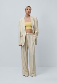 Beige pinstriped blazer and matching wide-leg pants over a yellow crop top. Blazer has a relaxed fit and subtle shoulder padding.