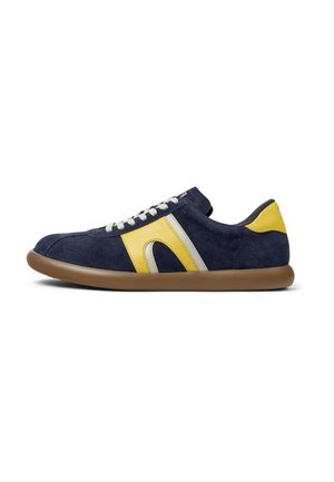 Marineblauwe suède sneaker met gele en zilveren accenten, ronde neus, beige rubberen zool en witte veters voor sluiting. Zijkant heeft een gebogen ontwerp.