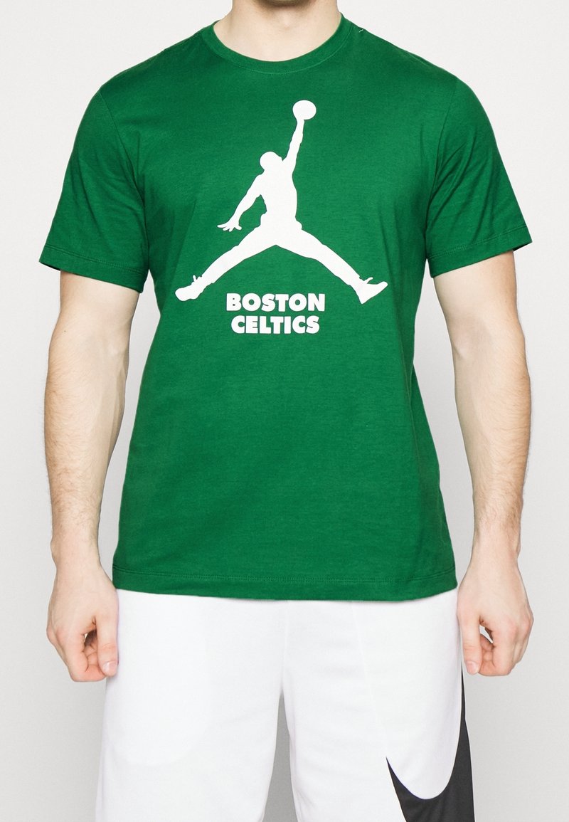 Mies, joka pukeutuu vihreään t-paitaan, jossa on valkoinen koripalloilijan siluetti ja teksti "Boston Celtics", parina valkoiset shortsit, joissa on musta swoosh.