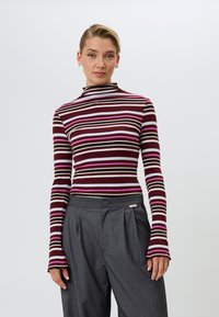 Langsleeve mock-neck top met multicolore strepen in bordeauxrood, roze en crème. Gepaarde met hooggetailleerde, grijze broek met streepjes.