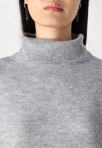 Suéter de cuello alto gris con un cuello acanalado, hecho de una tela suave y texturizada, que presenta un diseño sin costuras. Patrón de punto horizontal visible.