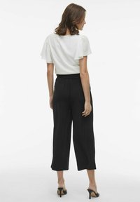 White blouse with flutter sleeves, paired with high-waisted black wide-leg pants. Smooth texture and ankle-length with open-toe heels.
