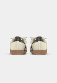 Crème-kleurige schoen met contrasterende donkere accenten, gestructureerde achterpaneel en rubberen zool; beschikt over gestikte details en een minimalistisch ontwerp.