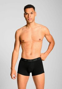 Black boxer briefs with elastic waistband featuring gray logo, snug fit, smooth texture, and mid-thigh length. Model is not wearing a shirt.