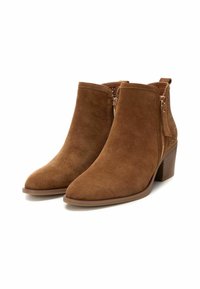 Botas de ante marrones hasta el tobillo con punta afilada, cremalleras laterales y un panel trasero texturizado. Tacón bajo apilado para mayor estabilidad.