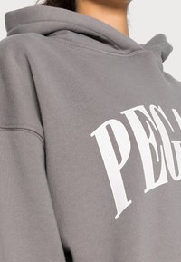 Grauer Hoodie aus weichem Material mit großem weißen Schriftzug "PEGAL" auf der Vorderseite. Klassische, verstellbare Kapuze mit Kordelzug.