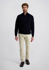 Marine blauw zip-up sweater met lange mouwen, gecombineerd met lichtbeige corduroy broeken en donkerbruine schoenen, gepresenteerd door een staande mannelijke model.